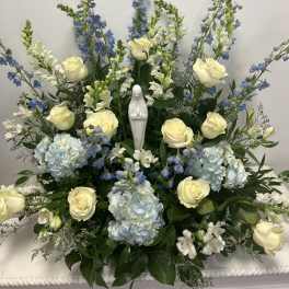 White roses and blue flowers arranged around a small statue
