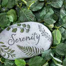 Decorative stone engraved with the word Serenity surrounded by green leaves