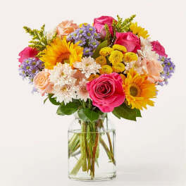 Mixed bouquet of roses, sunflowers, and daisies in a clear glass vase