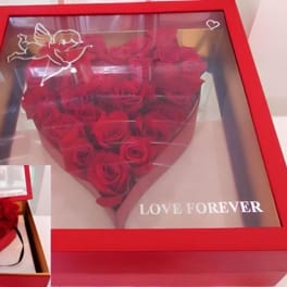 Red roses arranged in a heart-shaped gift box with a clear lid