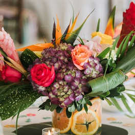 Tropical bouquet with roses, hydrangea, and bird of paradise in a citrus-decorated vase