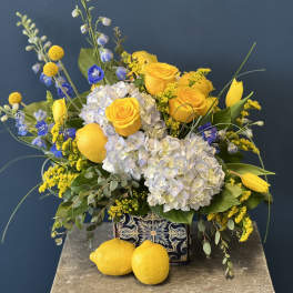 Yellow roses and white hydrangeas in a patterned ceramic vase with lemons