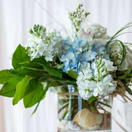 Blue and white flowers arranged in a glass vase with broad green leaves