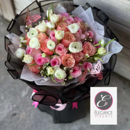 Round bouquet of pink, peach, and white roses and ranunculus in black wrap with butterfly accents