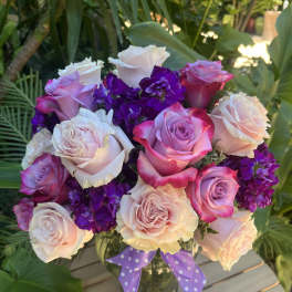 Bouquet of pink, white, and purple roses in a glass vase with a polka-dot ribbon
