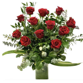 Arrangement of red roses with lush greenery in a clear cylinder vase