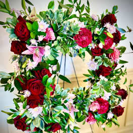 Standing wreath of red and pink flowers with lush green foliage on a metal easel.