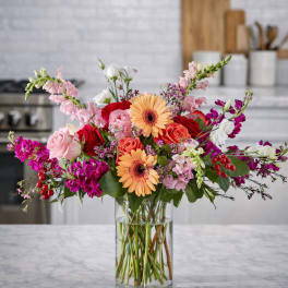 Mixed bouquet of roses, gerbera daisies, and pink blooms in a clear glass vase