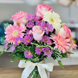 Pink roses and gerbera daisies in a glass vase with a white ribbon