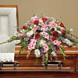 Casket spray of red roses, pink lilies, and mixed blooms arranged on a wooden casket