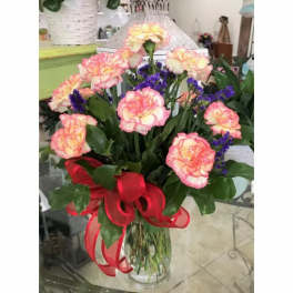 Bouquet of pink and yellow carnations with purple filler in a clear vase