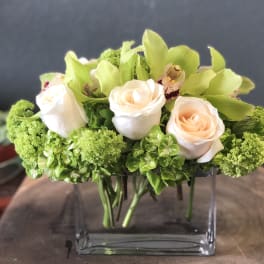 Compact bouquet of pale peach roses and green orchids in a clear glass vase