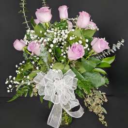 Pink roses and baby's breath in a glass vase with a white bow