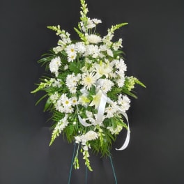 Tall standing spray of white flowers with a white ribbon on an easel stand