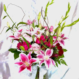 Pink lilies and roses in a glass vase with a ribbon