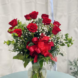 Red roses arranged in a glass vase with a red ribbon
