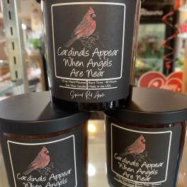 Three black-lidded candles with cardinal labels and memorial text