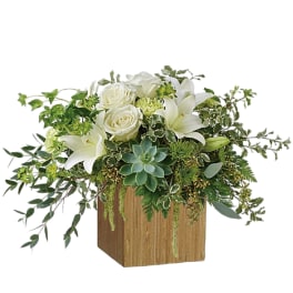 White roses and lilies in a wooden cube vase with trailing greenery