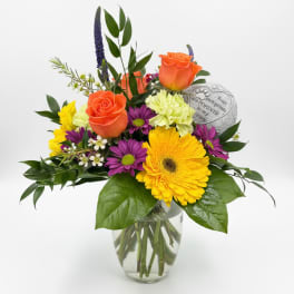 Mixed bouquet with orange roses, yellow gerbera daisies, and purple flowers in a glass vase