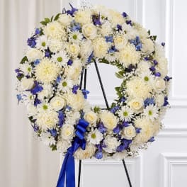 White and blue floral wreath on a stand with a blue ribbon