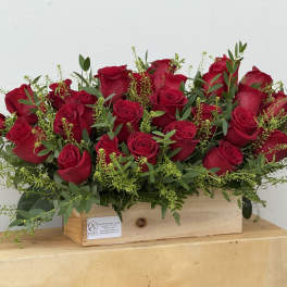 Red roses arranged in a wooden box with greenery