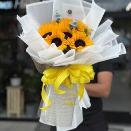 Bouquet of bright yellow sunflowers wrapped in white paper with a yellow ribbon