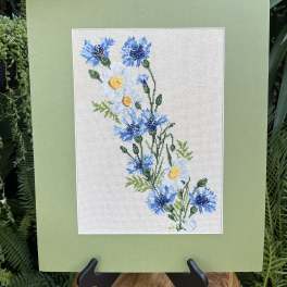 Framed floral embroidery with blue and white flowers on a pale green mat