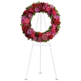 Circular floral wreath on a white easel with pink and red blooms