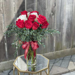 Red and white roses in a clear glass vase with a red ribbon
