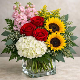 Bouquet of red roses, sunflowers, pink blooms, and white hydrangea in a glass vase