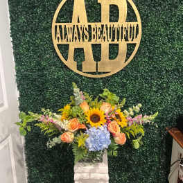 Arrangement of sunflowers, peach roses, and blue hydrangea on a pedestal