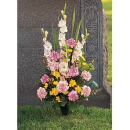 Standing funeral spray with pink and yellow flowers beside a gravestone