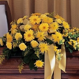 Yellow floral casket spray with ribbon on a wooden casket