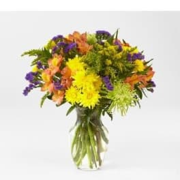 Mixed bouquet of yellow, orange, and purple flowers in a clear glass vase