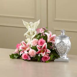 Pink floral arrangement with lilies and roses beside a silver urn and angel figurine