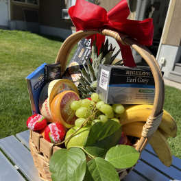 Gift basket with fruit, tea, cheese, and chocolates tied with a red bow