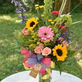 Mixed bouquet with sunflowers, pink gerberas, and roses in a glass vase