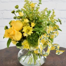 Yellow roses and daisies in a round glass vase with a yellow ribbon