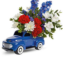 Blue toy truck holding a red, white, and blue flower arrangement