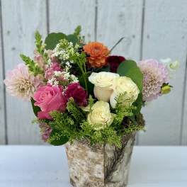 Mixed bouquet of pink, white, and orange flowers in a birch-style container