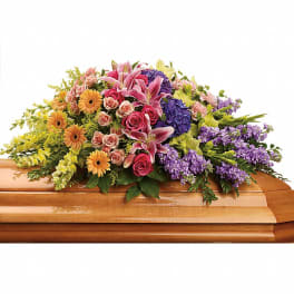 Colorful floral casket spray with roses, lilies, gerberas, and purple blooms