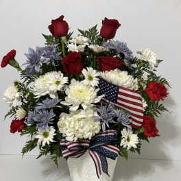 Red roses and white daisies in a white vase with an American flag ribbon