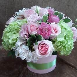 Pink roses and green hydrangeas arranged in a round box.