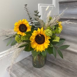 Sunflower arrangement in a glass vase with green accents and dried grasses