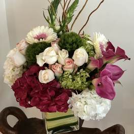 Mixed bouquet in a square glass vase with roses, hydrangea, gerbera daisies, and calla lilies