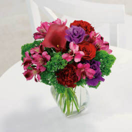 Mixed bouquet of red, pink, and purple flowers in a clear glass vase