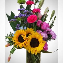 Mixed bouquet with sunflowers, carnations, and lilies in a glass vase