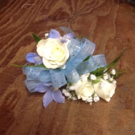 Two small rose arrangements with blue ribbon and purple petals on a wooden surface
