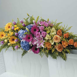 Colorful casket spray of mixed flowers in pink, orange, yellow, and blue on a white casket