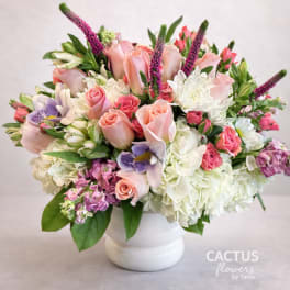 Mixed bouquet of pink roses, white hydrangeas, and purple flowers in a white vase